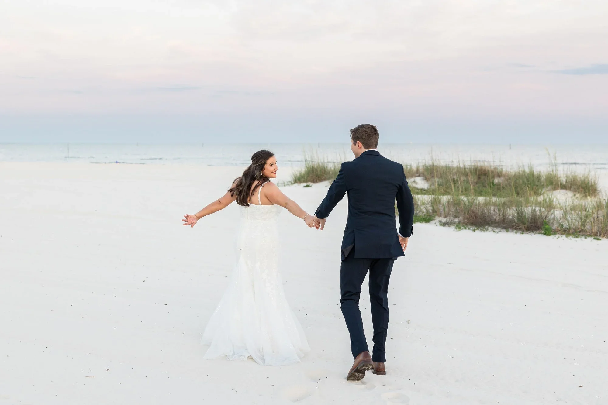 Bride and groom holding hands walking on a sandy beach at sunset