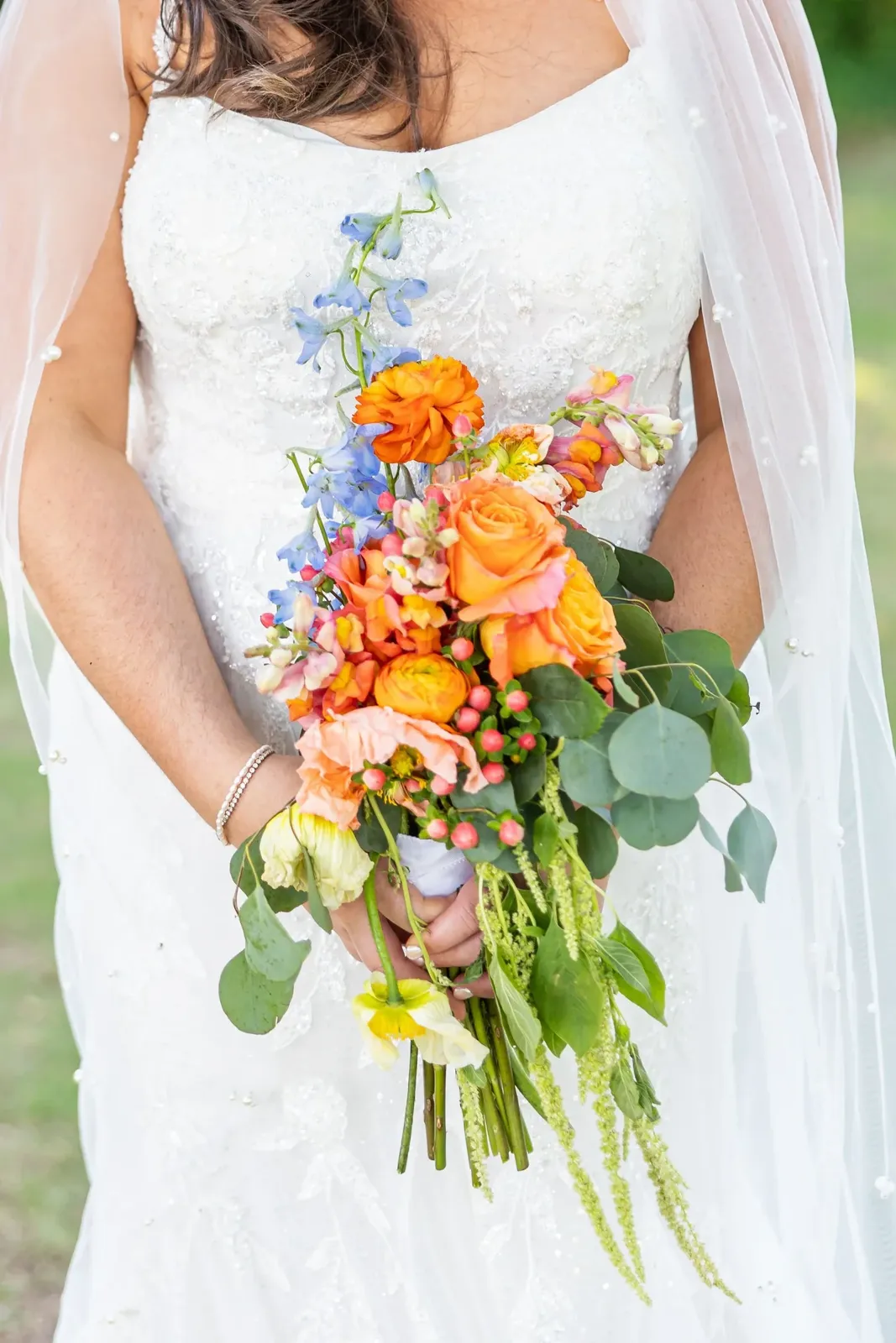 Bride holding a vibrant bouquet with orange, pink and blue flowers